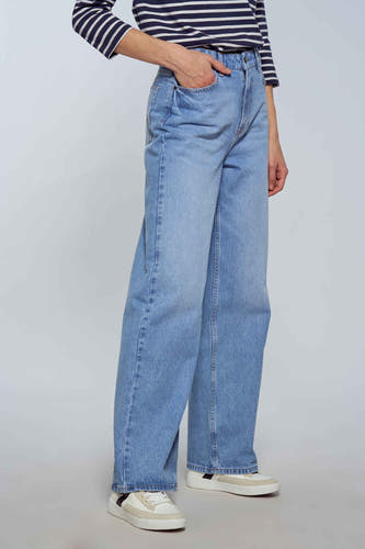 Jean décontracté de denim bleu clair de Le Fabuleux Marcel de Bruxelles, associé à une chemise rayée et des baskets blanches.