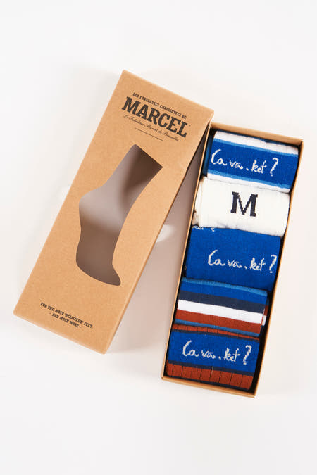 Chaussettes multicolores de Le Fabuleux Marcel de Bruxelles, emballées dans une boîte avec une découpe en forme de pied et une inscription.