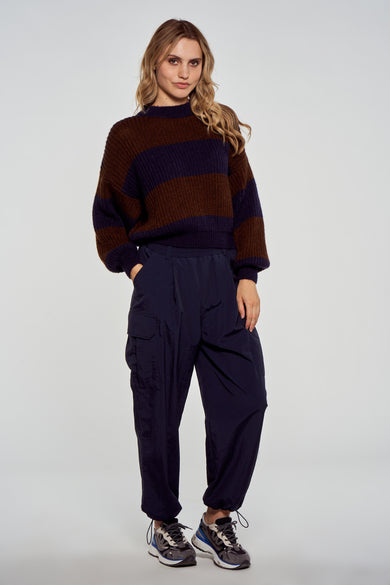 Pantalon cargo bleu de Le Fabuleux Marcel de Bruxelles, avec poches et resserré aux chevilles, porté avec un pull rayé et des baskets.