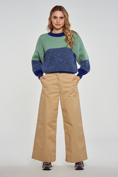 Pull multicolore en maille à col rond de Le Fabuleux Marcel de Bruxelles, blocs verts et bleus, coupe ample, modèle de face, pantalon beige et baskets.