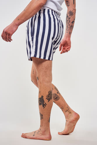 Blauwe zwembroek van Le Fabuleux Marcel de Bruxelles, met verticale strepen en tatoeages op de benen.
