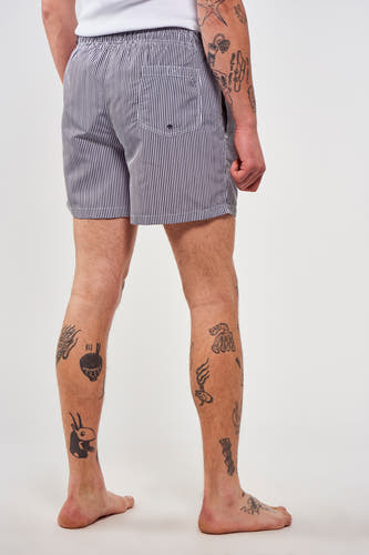 Blauw gestreepte zwembroek van Le Fabuleux Marcel de Bruxelles, met tatoeages op de benen.
