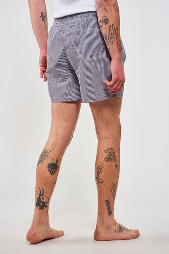 Blauw gestreepte zwembroek van Le Fabuleux Marcel de Bruxelles, met een elastische tailleband en tatoeages op de benen.
