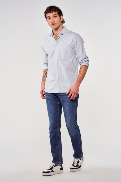 Blauw overhemd met lange mouwen van Le Fabuleux Marcel de Bruxelles, gedragen met donkerblauwe jeans en witte sneakers.