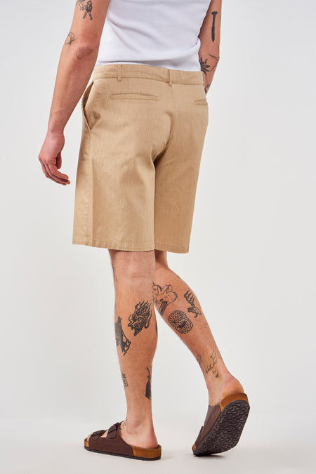 Bruine short van Le Fabuleux Marcel de Bruxelles, met achterzakken, gedragen met een wit hemd en sandalen.
