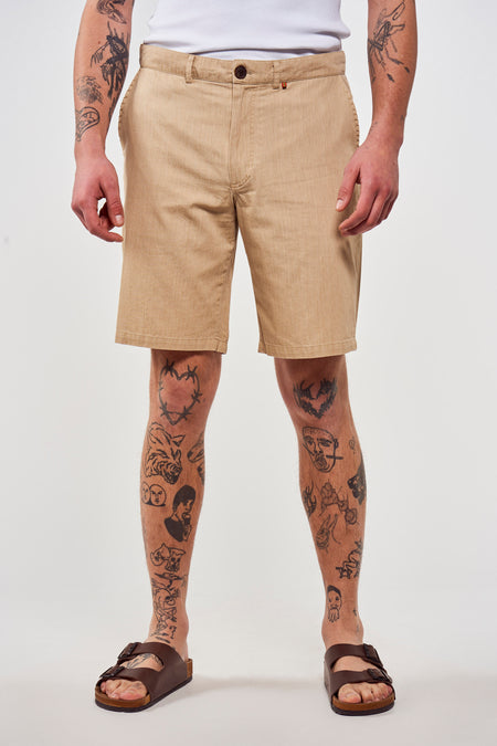 Short brune de Le Fabuleux Marcel de Bruxelles, avec des tatouages sur les jambes et des sandales brunes.