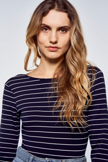 T-shirt bleu à manches longues avec rayures blanches de Le Fabuleux Marcel de Bruxelles, porté par un mannequin aux cheveux ondulés et jean, gros plan avant.