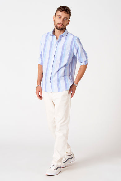 Blauw gestreept overhemd met korte mouwen van Le Fabuleux Marcel de Bruxelles, met lichte crèmekleurige broek en witte sneakers.

