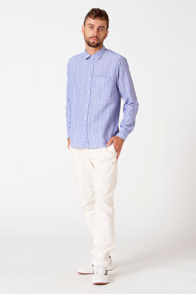 Blauw gestreept overhemd met lange mouwen van Le Fabuleux Marcel de Bruxelles, gedragen met crèmekleurige broek en witte sneakers.