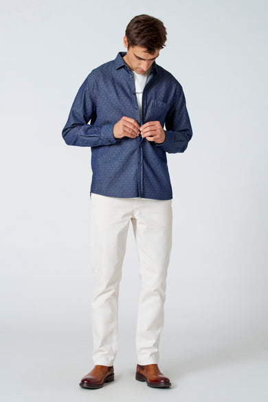 Blauw overhemd met lange mouwen van Le Fabuleux Marcel de Bruxelles, met een subtiel stippenpatroon, gedragen met een wit T-shirt, crèmekleurige broek en bruine laarzen.
