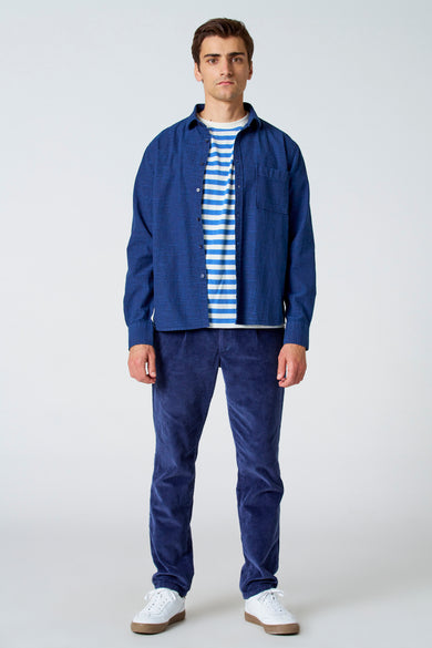 Blauw, linnen overhemd met lange mouwen van Le Fabuleux Marcel de Bruxelles, gedragen over gestreept shirt met corduroy broek en witte sneakers.
