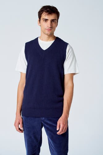 Blauwe debardeur van Le Fabuleux Marcel de Bruxelles, met ribgebreide boord, gedragen over een gestreept shirt en blauwe corduroy broek.