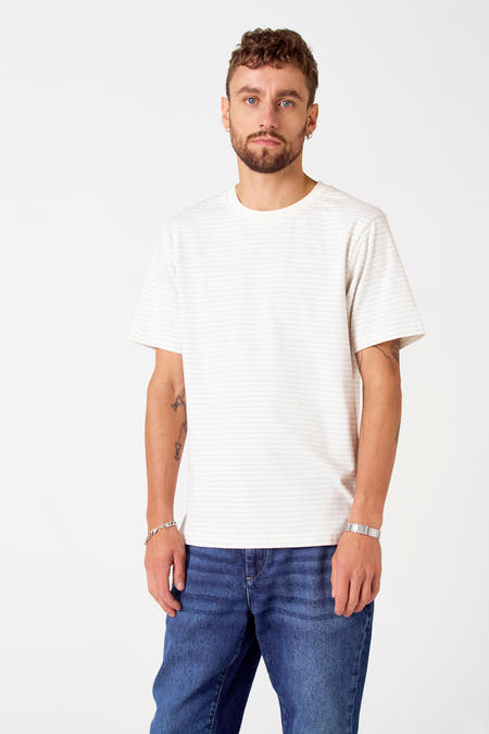 Grijs T-shirt met korte mouwen van Le Fabuleux Marcel de Bruxelles, met subtiele horizontale strepen, gedragen met blauwe jeans en zilveren sieraden.
