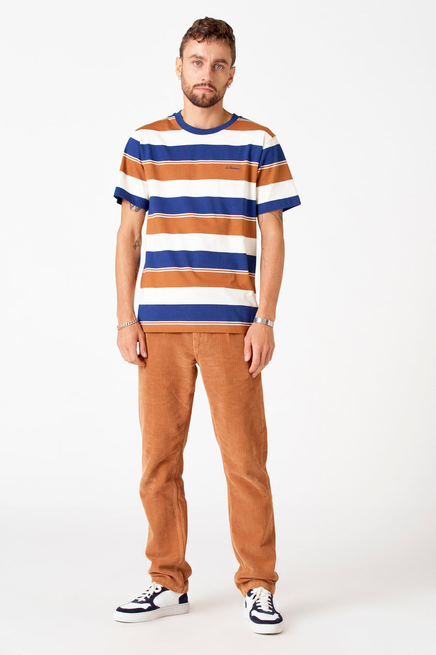 T-shirt multicolore à manches courtes de Le Fabuleux Marcel de Bruxelles, avec des rayures horizontales, porté avec un pantalon corduroy marron et des baskets blanches.