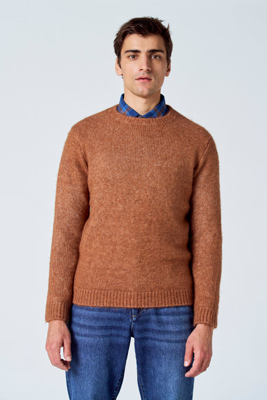 Bruine trui met ronde hals van Le Fabuleux Marcel de Bruxelles, gedragen over een blauw geruit overhemd en een blauwe jeans.