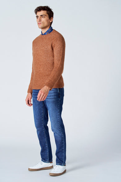 Bruine trui met ronde hals van Le Fabuleux Marcel de Bruxelles, gedragen met een blauw geruit overhemd en blauwe jeans, zij aanzicht.
