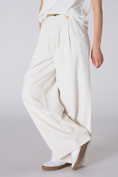 Witte jeansbroek van Le Fabuleux Marcel de Bruxelles, met plooien en bruine accenten, gecombineerd met witte sneakers.