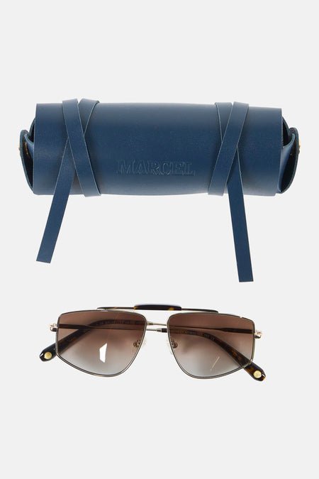 Lunettes de soleil dorées de Le Fabuleux Marcel de Bruxelles avec verres marron, posées devant un étui de rangement en cuir bleu foncé.