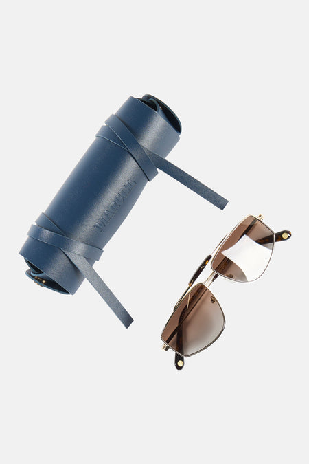 Gouden zonnebril van Le Fabuleux Marcel de Bruxelles met bruine glazen, naast een opgerolde blauwe leren etui met de naam 'MARCEL' erin gestanst.