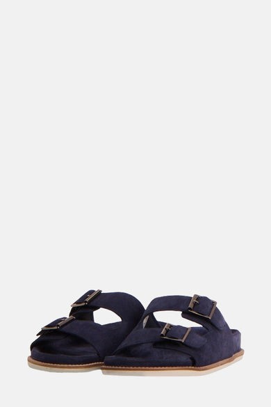 Blauwe slippers van Le Fabuleux Marcel de Bruxelles, met dubbele gespsluiting en een platte zool.
