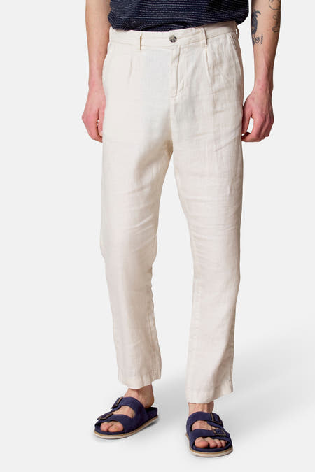 Beige kostuumbroek van Le Fabuleux Marcel de Bruxelles, met plooien en blauwe sandalen.
