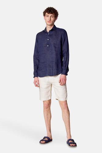 Man met donkerblauw linnen overhemd, witte shorts en blauwe sandalen, staand.