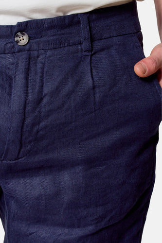 Close-up marineblauwe linnen broek met knoop en hand in zak.