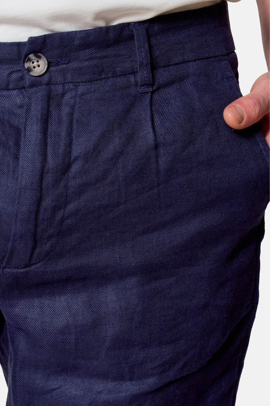 Close-up marineblauwe linnen broek met knoop en hand in zak.
