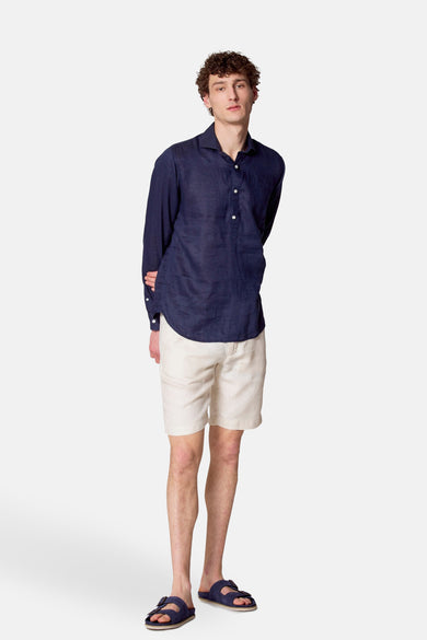 Blauw overhemd met lange mouwen van Le Fabuleux Marcel de Bruxelles, gedragen met witte linnen shorts en blauwe sandalen.
