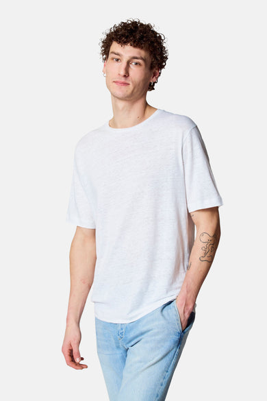 T-shirt blanc à manches courtes de Le Fabuleux Marcel de Bruxelles, porté avec un jean et un tatouage cartoon sur le bras.
