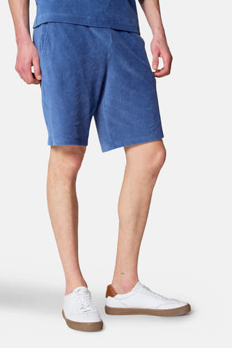 Short en cotonnade bleu de Le Fabuleux Marcel de Bruxelles, porté par un modèle avec des baskets blanches.