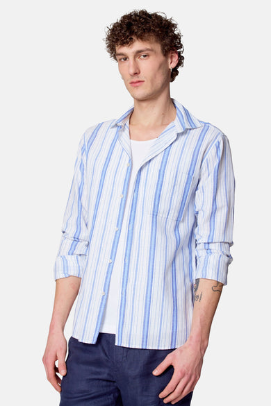 Blauw gestreept overhemd met lange mouwen van Le Fabuleux Marcel de Bruxelles, gedragen over een wit T-shirt en donkerblauwe broek.