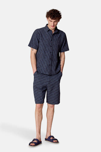 Shorts bleus de Le Fabuleux Marcel de Bruxelles, avec un motif floral et portés avec une chemise coordonnée et des sandales.