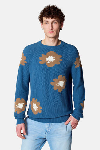 Blauwe trui met ronde hals van Le Fabuleux Marcel de Bruxelles, met bloemenmotief en lange mouwen, gecombineerd met een lichtblauwe jeans.
