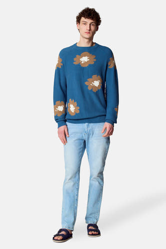 Blauwe trui met ronde hals van Le Fabuleux Marcel de Bruxelles, met bruine en witte bloemenprint, gecombineerd met lichte jeans en sandalen.
