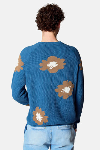 Blauwe trui met ronde hals van Le Fabuleux Marcel de Bruxelles, met bloempatroon en een lichte jeans.
