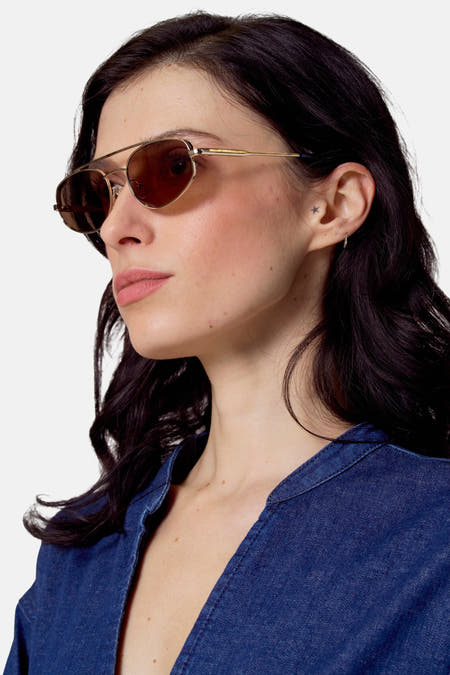 Gouden zonnebril van Le Fabuleux Marcel de Bruxelles, gedragen door een vrouw met een blauw denim shirt.