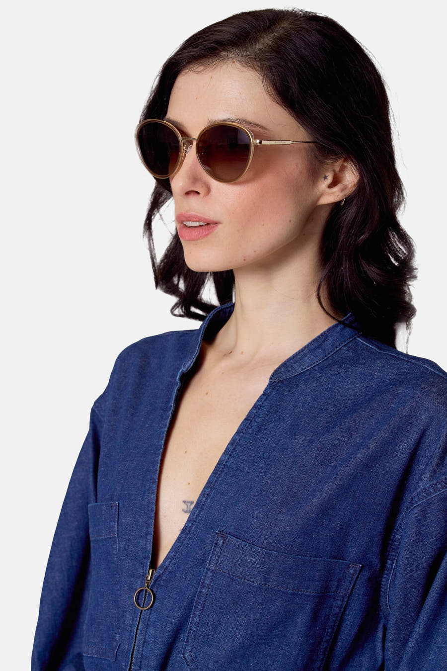 Beige zonnebril van Le Fabuleux Marcel de Bruxelles, met gouden montuur en denim jumpsuit.
