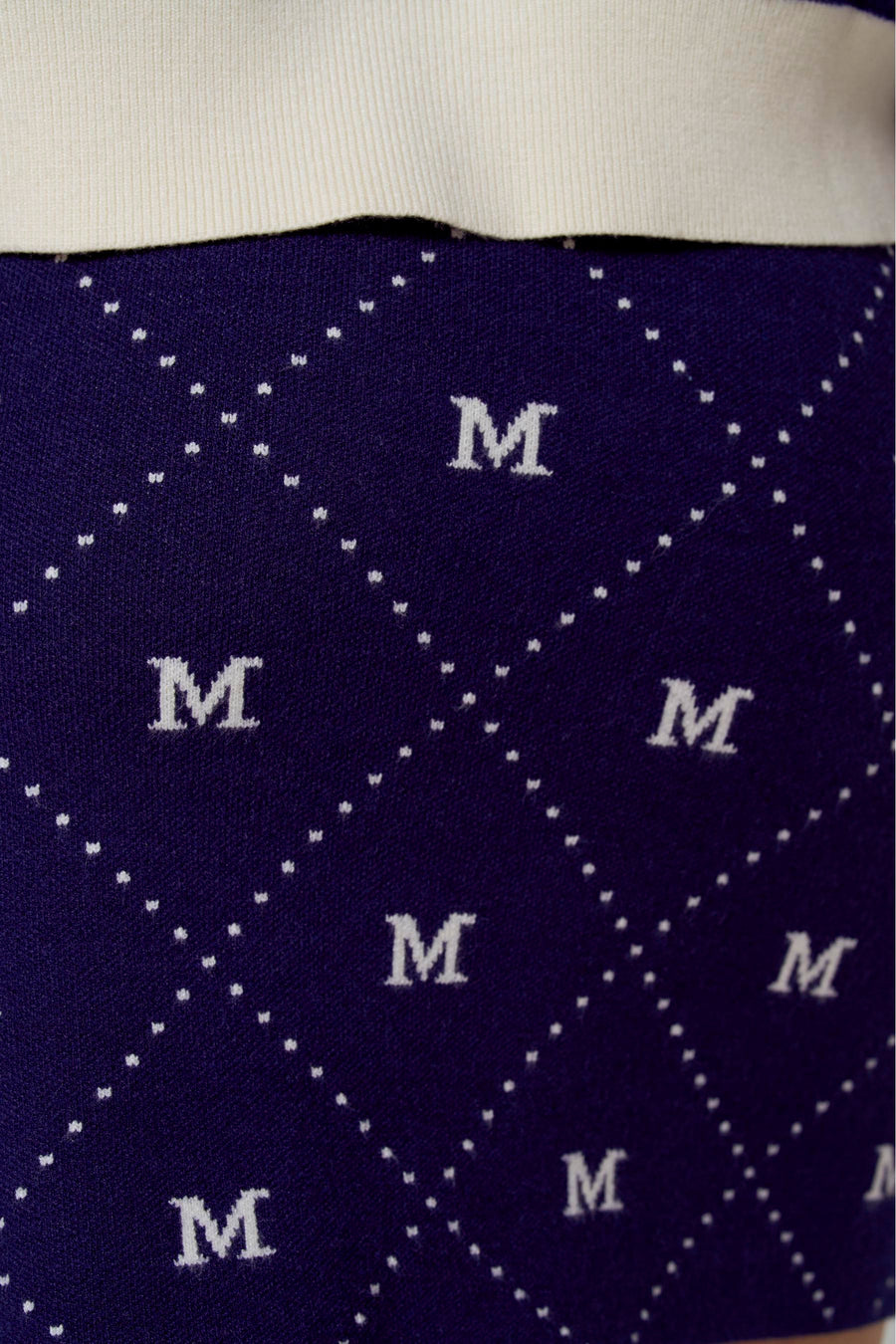 Jupe courte bleue de Le Fabuleux Marcel de Bruxelles, avec un motif 'M' blanc et des carreaux à pois.