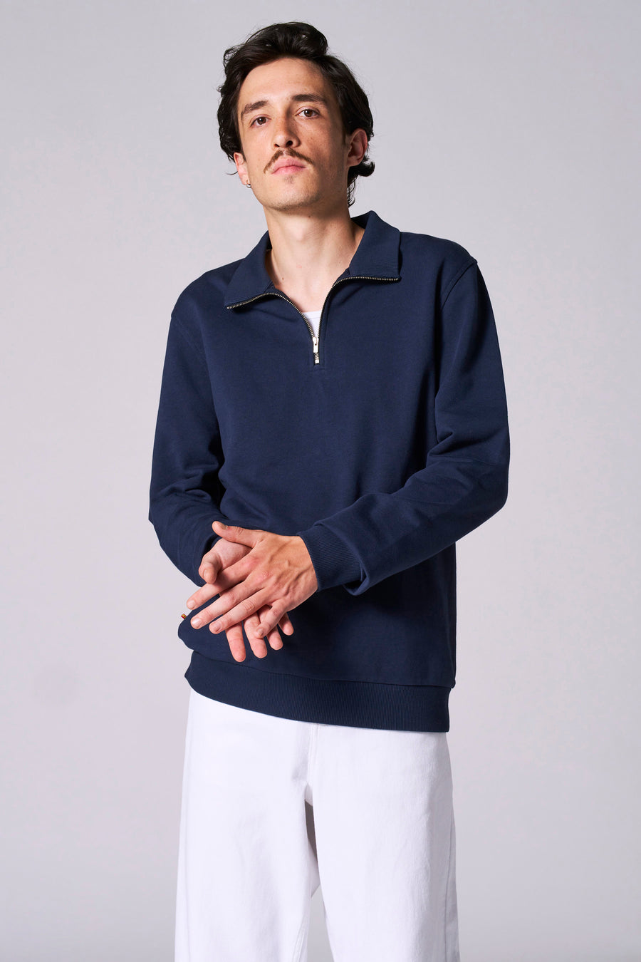 Man, blauwe sweater met rits, witte broek, staand.
