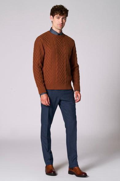 Bruine trui met ronde hals van Le Fabuleux Marcel de Bruxelles, met kabelpatroon, gecombineerd met blauwe pantalon en bruine leren schoenen.
