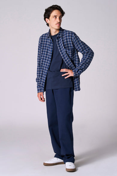 Man in blauwe outfit met geruit overhemd en witte sneakers.