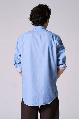 Chemise bleue à manches longues de Le Fabuleux Marcel de Bruxelles, vue de derrière, avec des manches retroussées.
