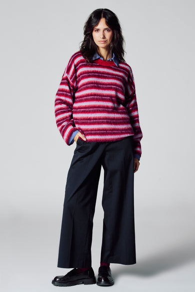 Pull multicolore à col rond de Le Fabuleux Marcel de Bruxelles, à rayures, associé à une chemise bleue et un pantalon noir large.