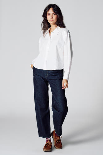 Chemise blanche à longues manches de Le Fabuleux Marcel de Bruxelles, portée avec des jeans foncés et des chaussures marrons.