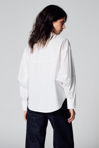 Chemise blanche à manches longues de Le Fabuleux Marcel de Bruxelles, vue de dos, associée à des jeans foncés.