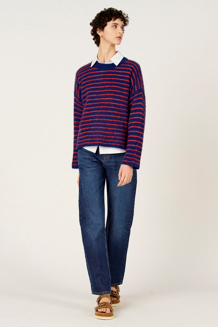 Multikleurige trui met ronde hals van Le Fabuleux Marcel de Bruxelles, met horizontale strepen en gecombineerd met een wit overhemd en jeans.
