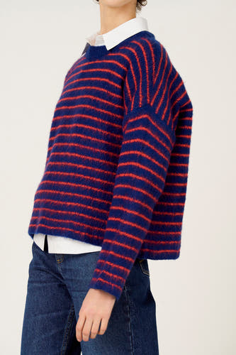 Multikleurige trui met ronde hals van Le Fabuleux Marcel de Bruxelles, met rode strepen, gecombineerd met een wit overhemd en een blauwe jeans.
