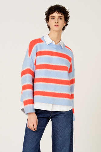 Pull multicolore à col rond de Le Fabuleux Marcel de Bruxelles, motif rayé bleu et orange, porté sur une chemise blanche, avec un jean foncé.