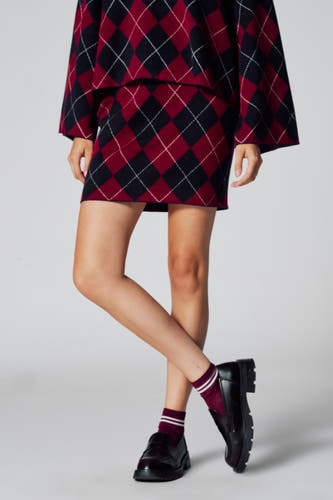 Korte multicolor rok van Le Fabuleux Marcel de Bruxelles, met ruitpatroon, gecombineerd met bordeaux sokken en zwarte schoenen.
